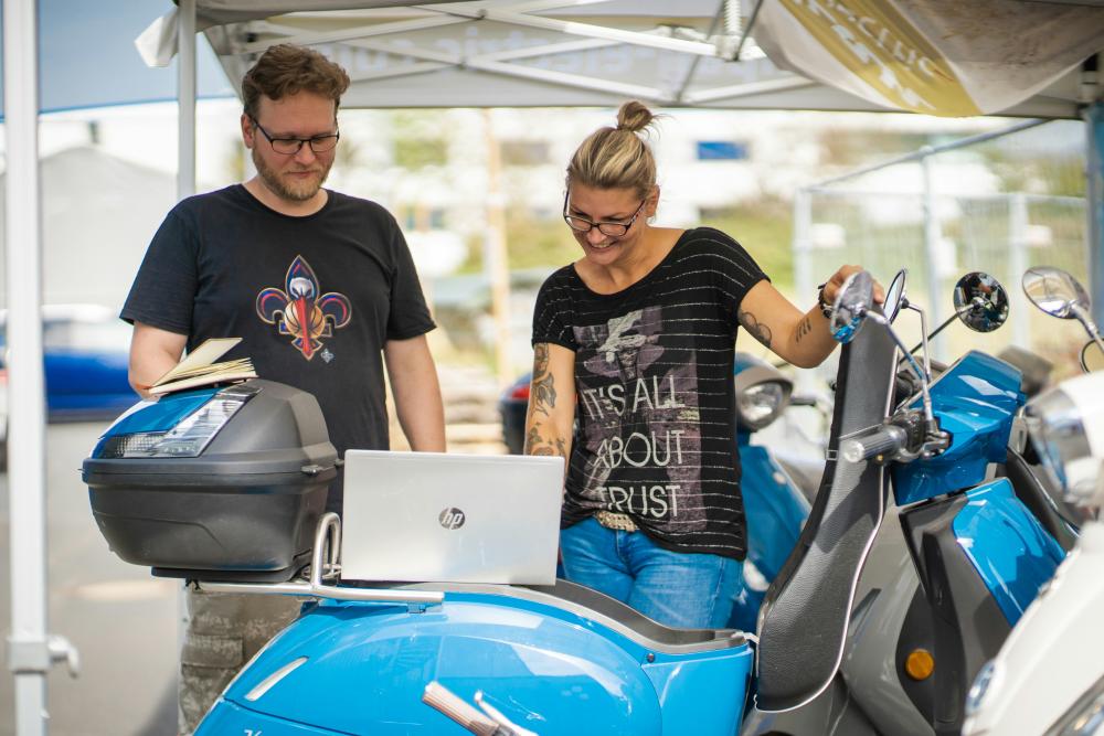 Two people look ta a laptop on a electronic scooter